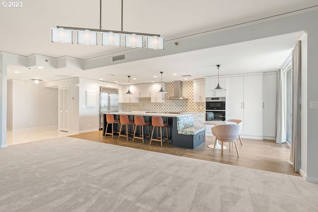 kitchen with a kitchen breakfast bar, a kitchen island, wall chimney exhaust hood, backsplash, and hanging light fixtures