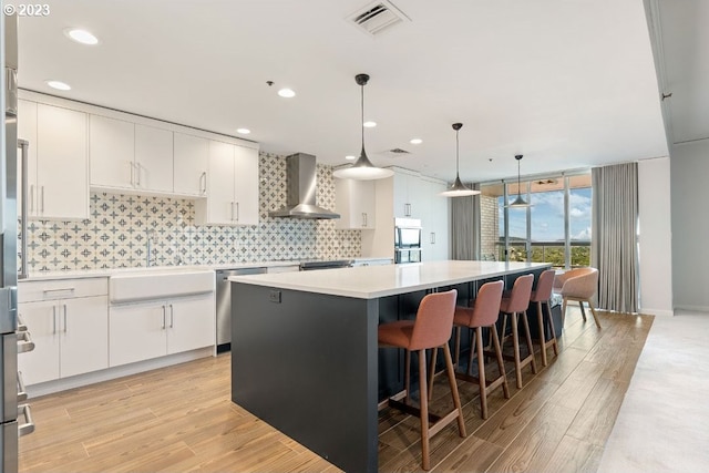 kitchen with pendant lighting, a kitchen island, wall chimney exhaust hood, white cabinetry, and backsplash