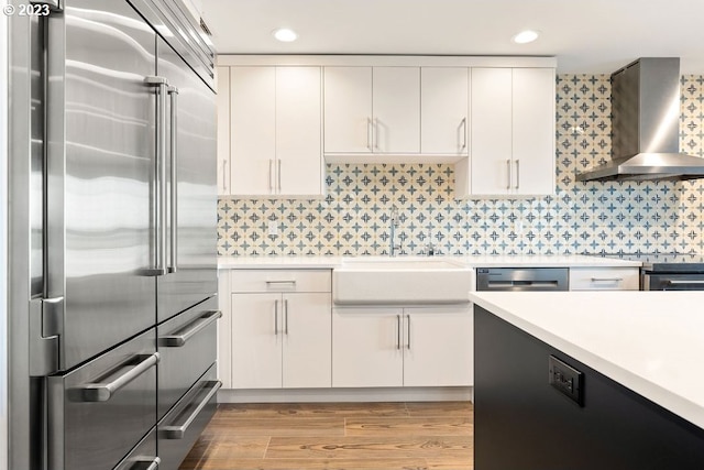 kitchen featuring white cabinetry, light hardwood / wood-style floors, stainless steel appliances, wall chimney range hood, and tasteful backsplash