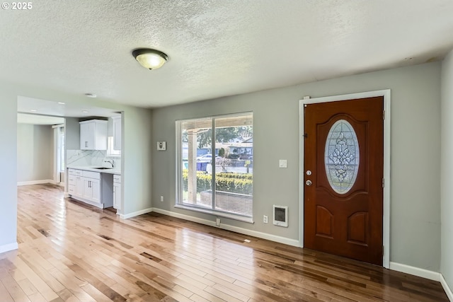 foyer entrance with heating unit, sink, a textured ceiling, and light wood-type flooring