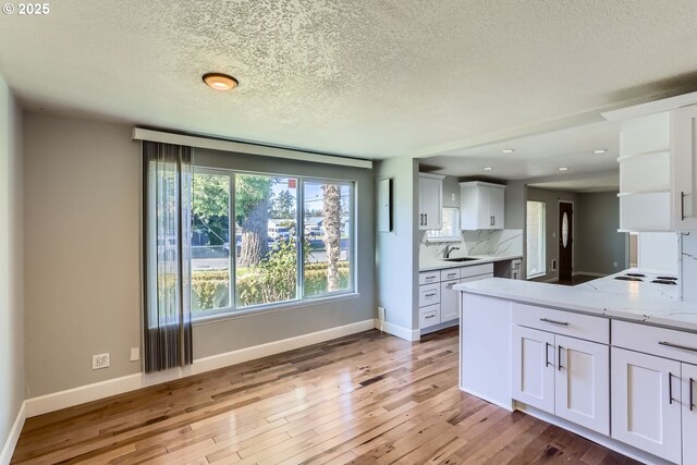 kitchen with white cabinetry, light stone countertops, sink, and light wood-type flooring