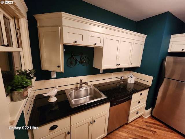 kitchen with appliances with stainless steel finishes, white cabinets, light hardwood / wood-style flooring, backsplash, and sink