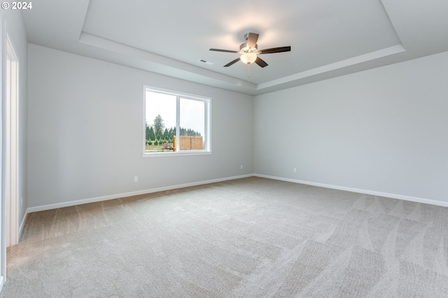 carpeted empty room with a raised ceiling and ceiling fan