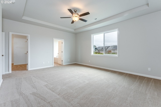 unfurnished bedroom featuring a raised ceiling, connected bathroom, light carpet, and ceiling fan