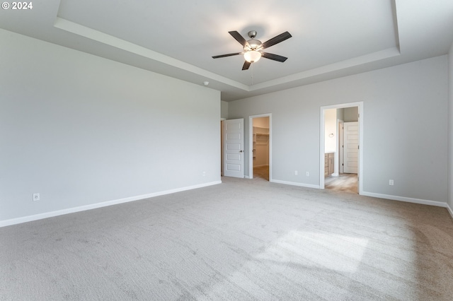 unfurnished bedroom with a tray ceiling, a walk in closet, and carpet flooring