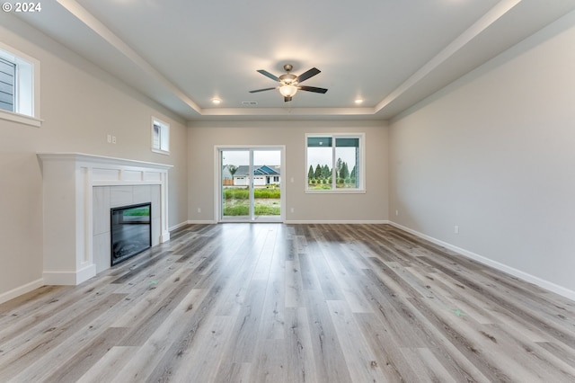 unfurnished living room with a tile fireplace, a raised ceiling, ceiling fan, and light hardwood / wood-style flooring