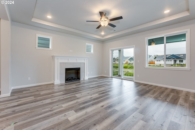 unfurnished living room with light hardwood / wood-style flooring, ceiling fan, a raised ceiling, and a fireplace