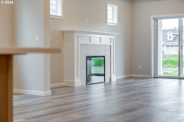 unfurnished living room with light wood-type flooring, a tiled fireplace, and plenty of natural light