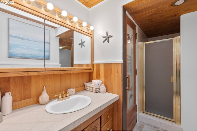 full bath featuring wooden ceiling, wooden walls, a wainscoted wall, vanity, and a shower stall