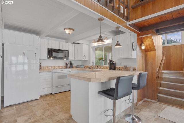 kitchen featuring white appliances, tile counters, a peninsula, a healthy amount of sunlight, and beam ceiling