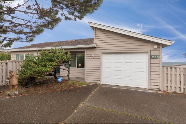 view of front of property featuring an attached garage, driveway, fence, and roof with shingles