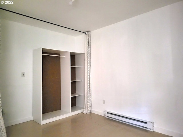 unfurnished bedroom with concrete floors, baseboard heating, and a closet