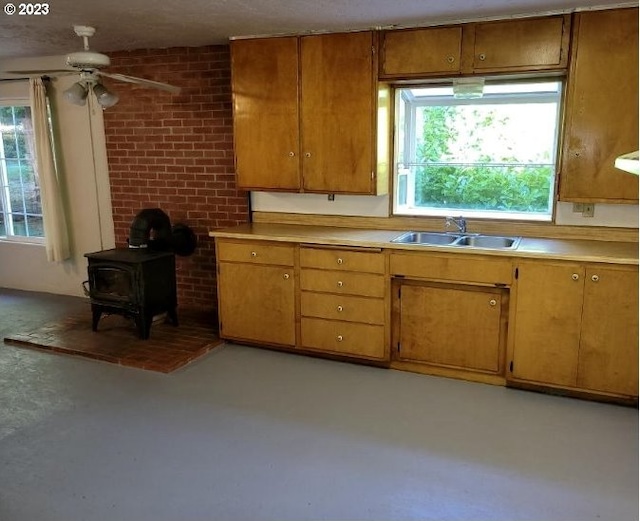 kitchen with brick wall, ceiling fan, concrete floors, a wood stove, and sink