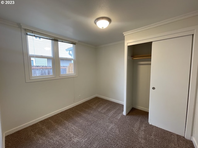 unfurnished bedroom featuring a closet, dark carpet, and ornamental molding