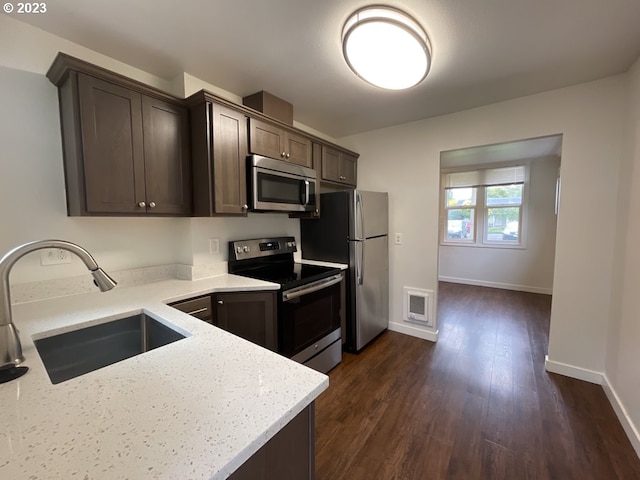 kitchen with light stone countertops, dark wood-type flooring, sink, stainless steel appliances, and dark brown cabinets