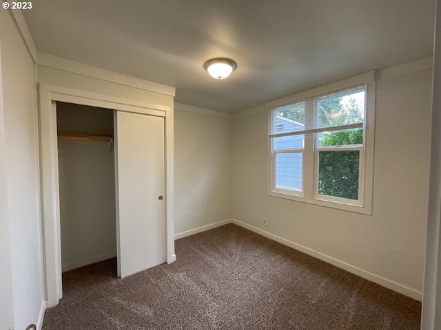 unfurnished bedroom with dark carpet and a closet