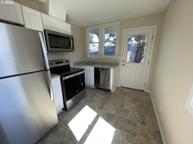 kitchen with white cabinetry, appliances with stainless steel finishes, dark tile floors, sink, and light stone counters