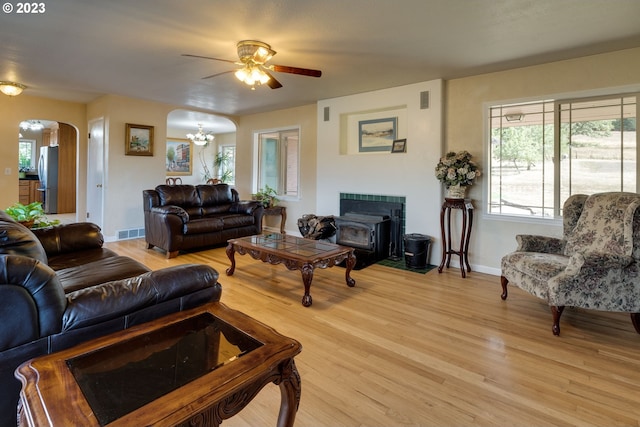 living room featuring a fireplace, a wood stove, ceiling fan with notable chandelier, and light wood-type flooring