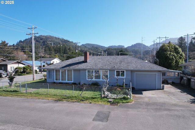 single story home featuring a fenced front yard, roof with shingles, a mountain view, a garage, and a front lawn