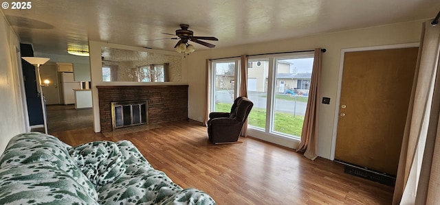 living room featuring a fireplace with flush hearth, ceiling fan, and wood finished floors