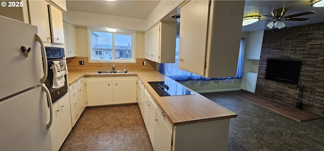 kitchen featuring a ceiling fan, a sink, black appliances, a fireplace, and backsplash