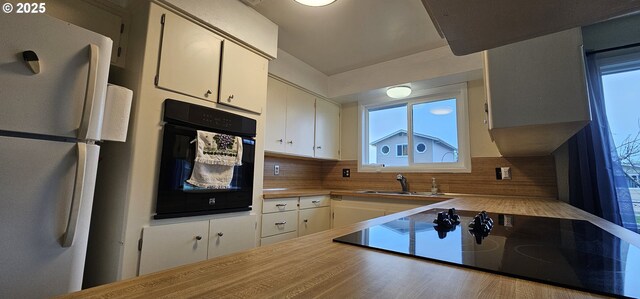 kitchen with black appliances, tasteful backsplash, white cabinets, and a sink