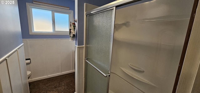 bathroom featuring a wainscoted wall, toilet, a shower with shower door, and a decorative wall