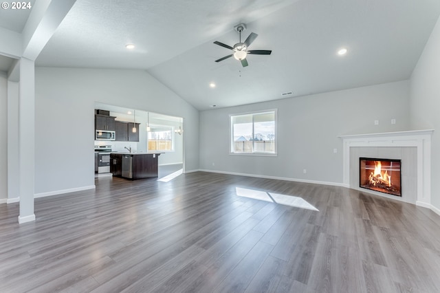 unfurnished living room with lofted ceiling, a tiled fireplace, wood-type flooring, and ceiling fan