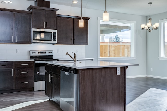 kitchen featuring appliances with stainless steel finishes, dark wood-type flooring, hanging light fixtures, and a center island with sink