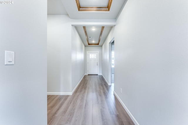 corridor with a tray ceiling and light wood-type flooring