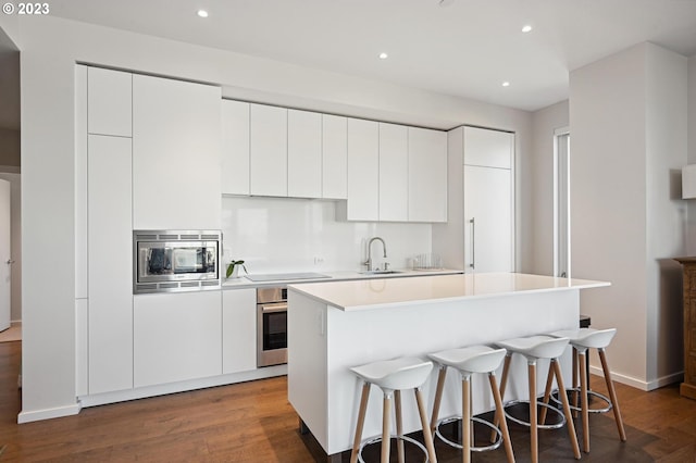 kitchen with a kitchen island, a breakfast bar area, stainless steel appliances, hardwood / wood-style flooring, and white cabinets