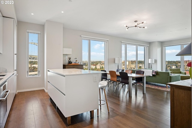 kitchen with an inviting chandelier, a breakfast bar, dark wood-type flooring, and white cabinetry