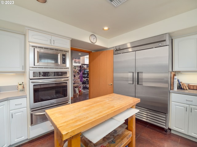 kitchen with dark tile flooring, built in appliances, and white cabinetry