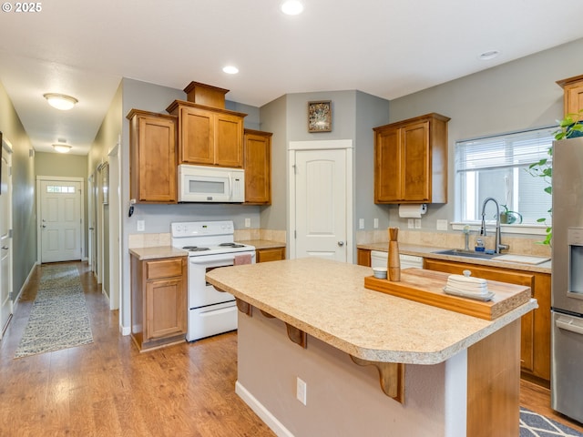 kitchen featuring a breakfast bar, light countertops, a kitchen island, light wood-type flooring, and white appliances