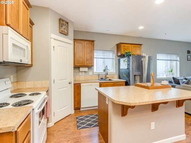 kitchen featuring white appliances, a center island, a sink, light countertops, and a wealth of natural light