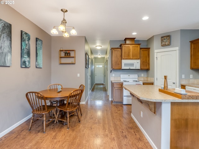 kitchen featuring brown cabinets, light countertops, hanging light fixtures, white appliances, and a kitchen breakfast bar