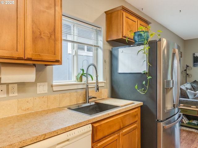 kitchen with a sink, light countertops, dishwasher, brown cabinetry, and stainless steel fridge