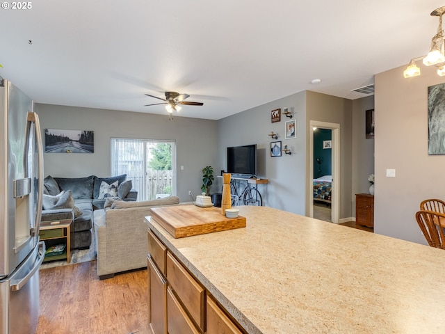 kitchen with pendant lighting, stainless steel refrigerator with ice dispenser, light countertops, light wood-style flooring, and open floor plan