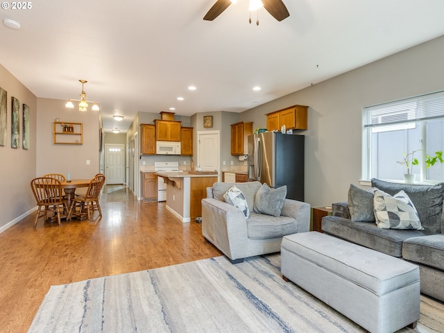 living area with recessed lighting, light wood-style flooring, baseboards, and ceiling fan with notable chandelier