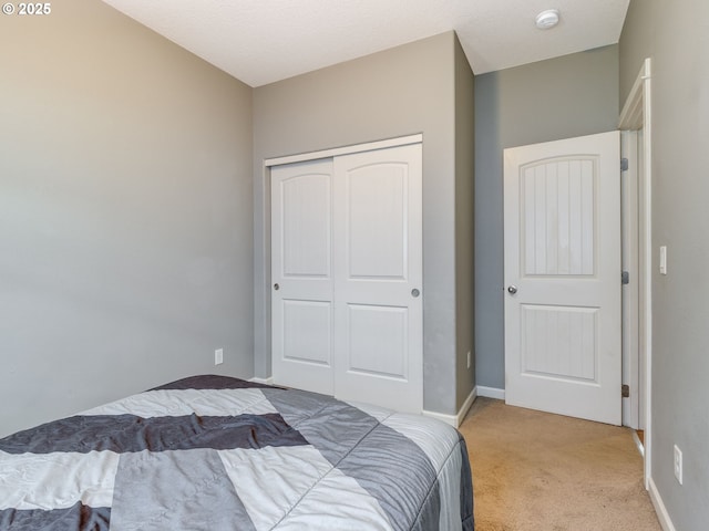 bedroom featuring baseboards, a closet, and light colored carpet