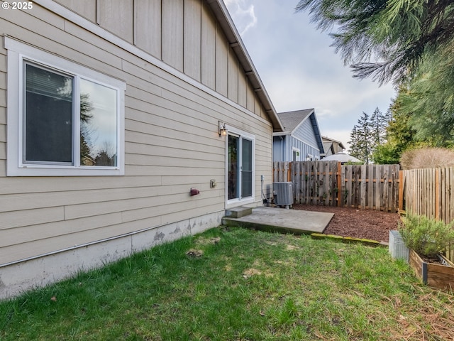 rear view of house with central AC unit, board and batten siding, a fenced backyard, and a lawn