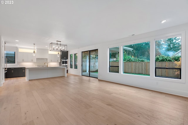 unfurnished living room with light hardwood / wood-style floors, sink, and a healthy amount of sunlight