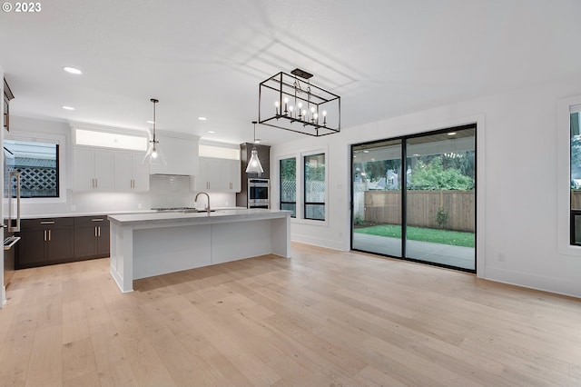 kitchen with light hardwood / wood-style floors, a kitchen island with sink, a breakfast bar area, white cabinetry, and pendant lighting