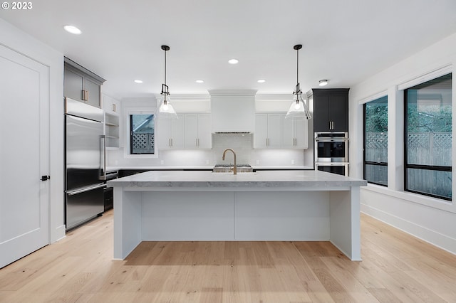 kitchen with light hardwood / wood-style flooring, stainless steel appliances, hanging light fixtures, tasteful backsplash, and an island with sink