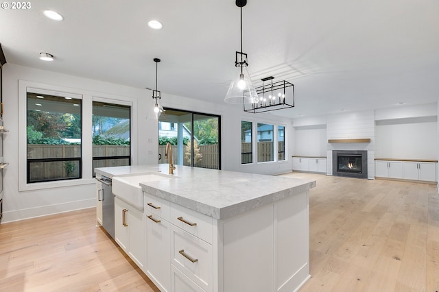 kitchen featuring hanging light fixtures, light hardwood / wood-style flooring, an island with sink, white cabinets, and a large fireplace