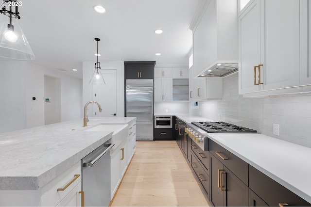 kitchen featuring light hardwood / wood-style floors, decorative light fixtures, backsplash, white cabinets, and appliances with stainless steel finishes