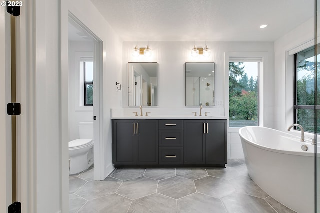 bathroom with tile flooring, a textured ceiling, a tub, double sink vanity, and toilet