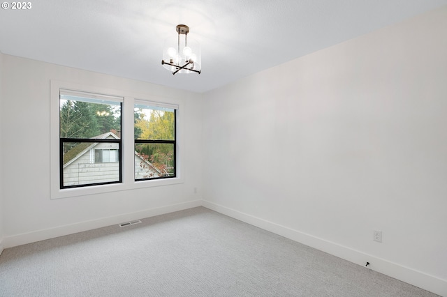 carpeted spare room with an inviting chandelier