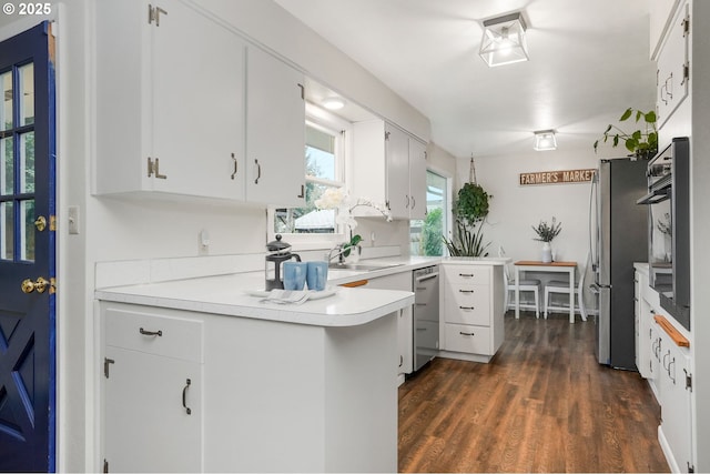 kitchen with white cabinetry, kitchen peninsula, appliances with stainless steel finishes, dark hardwood / wood-style floors, and sink