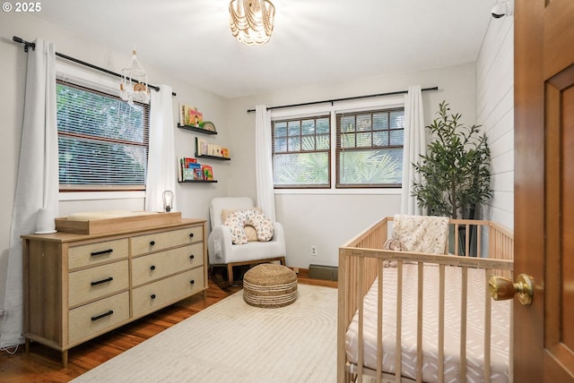 bedroom with dark wood-type flooring, a nursery area, and an inviting chandelier